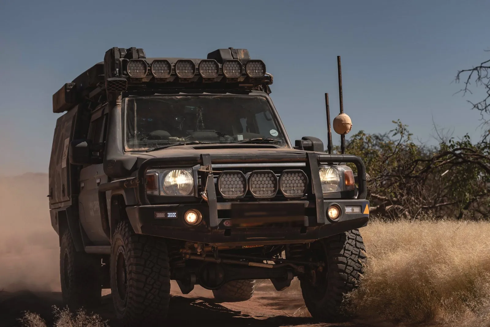 Front of a Land Cruiser 79 with a bull bar and driving lights, kicking up dust on a bush track