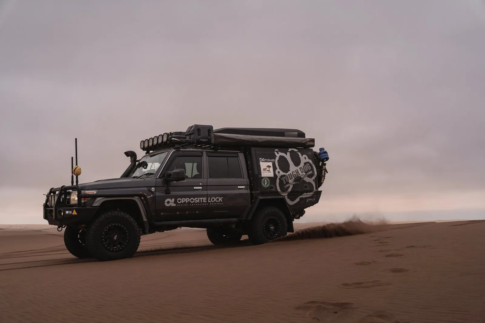 Side view of a kitted-out Land Cruiser 79 double cab driving across a dune